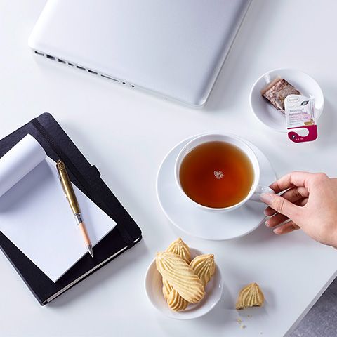 Tisch mit Teetasse, Laptop und Block mit Stift und Keksen in einer Schale
