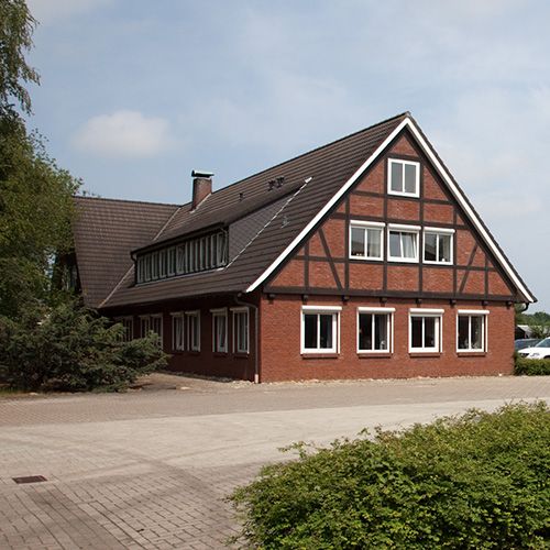 Backstein-Fachwerkhaus mit Satteldach in ländlicher Umgebung, umgeben von Bäumen.