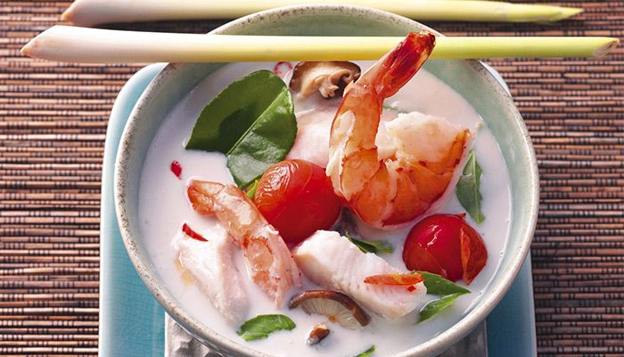 Thailändische Suppe mit Garnelen, Fisch, Tomaten, Pilzen und frischen Kräutern in Kokosmilch