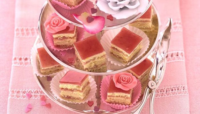 Etageren mit rosa glasierten Petit Fours, dekoriert mit Zuckerrosen und Herzkonfetti auf rosafarbener Tischdecke