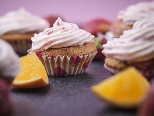 Cupcakes mit rosa-weißem Frosting, dekoriert mit Erdbeeren und Orangenschnitzen