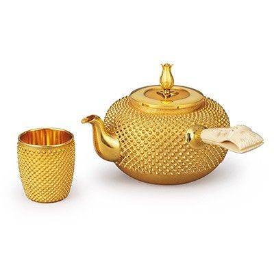 Goldene Teekanne mit passendem Teebecher auf weißem Hintergrund