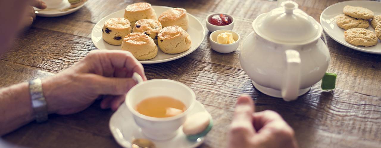 Traditionelle Teatime mit Scones, Clotted Cream, Marmelade und Tee auf einem Holztisch