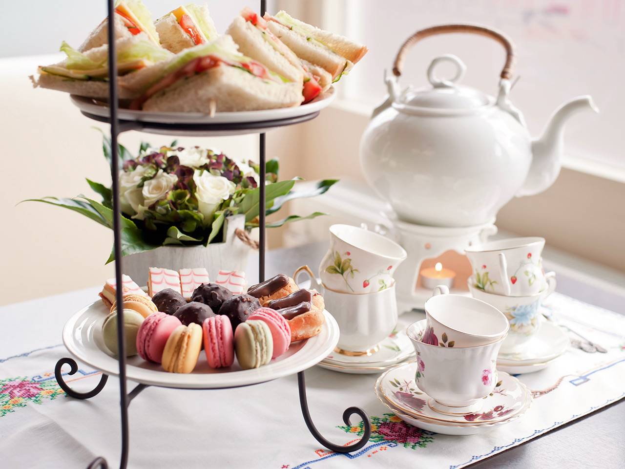 Elegant gedeckter Afternoon Tea mit Etageren voller Sandwiches, Macarons und Gebäck, dazu feines Porzellan-Geschirr und eine weiße Teekanne
