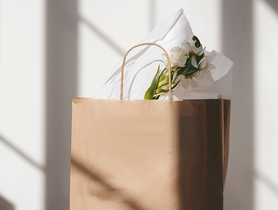 Kleine, braune Tütchen mit einem kleinen Blumenstrauß in hellem Sonnenlicht